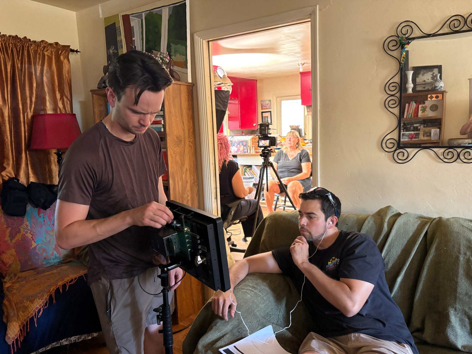 Kyle Wright, in a blue t-shirt on the couch with headphones, listens while a crew member adjusts the camera monitor.