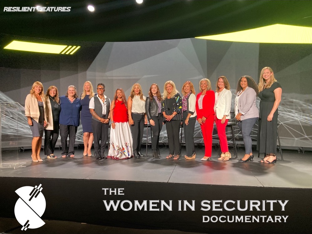A line of women standing together on a lit conference stage.