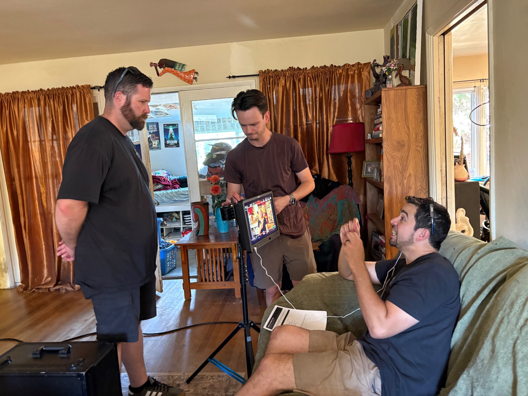 Kyle Wright, in a blue t-shirt on the couch, talks with two crew members standing at the camera monitor.