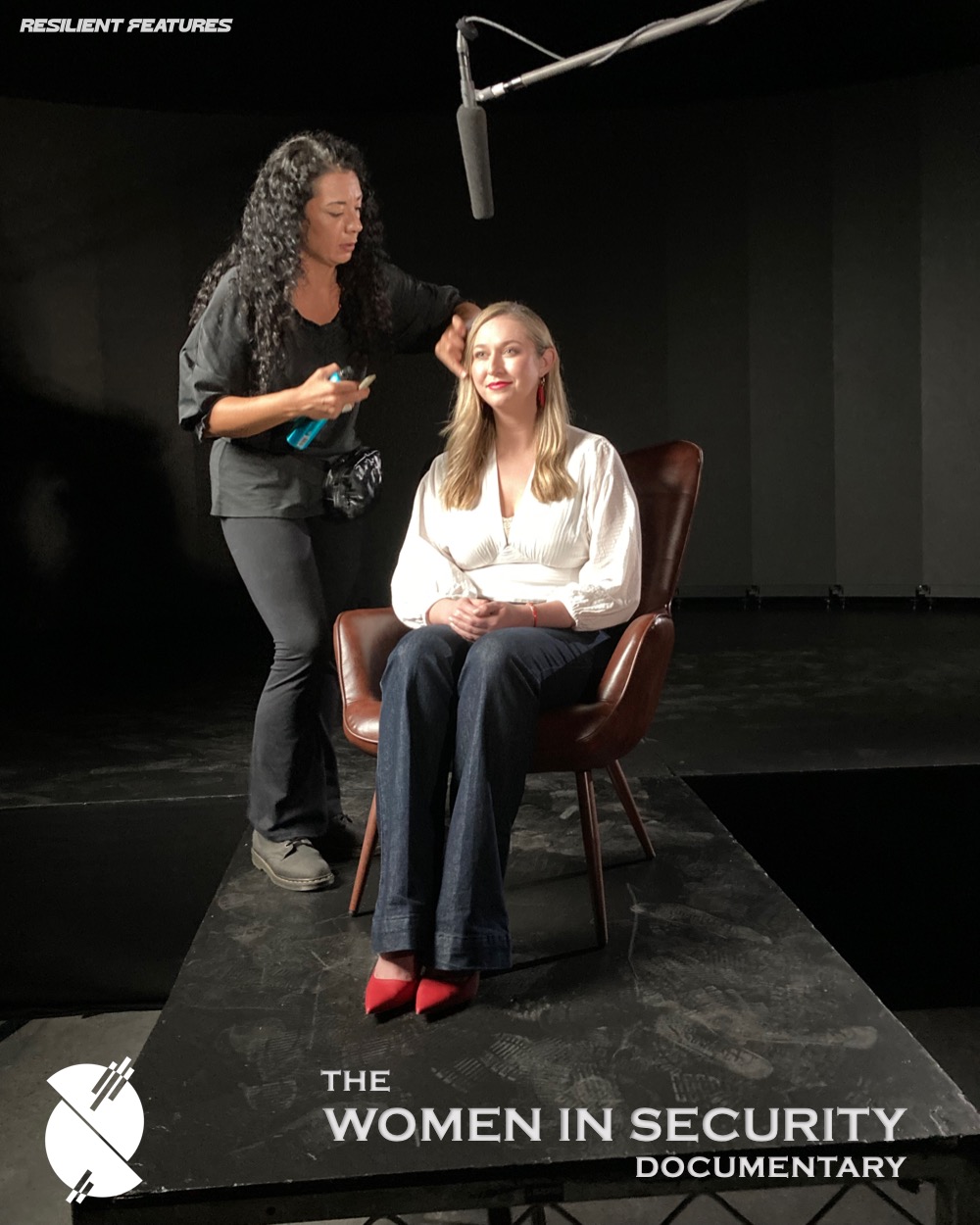 A stylist adjusting an interviewee's hair on the interview set, both lit by a single soft source.